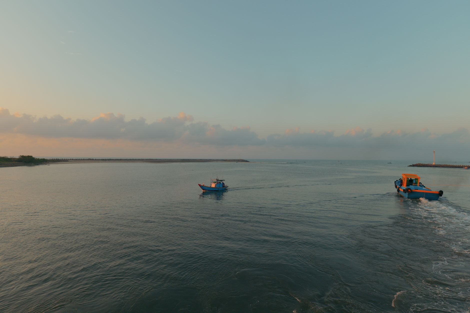 Two small fishing boats navigating serene waters under a soothing sunrise.